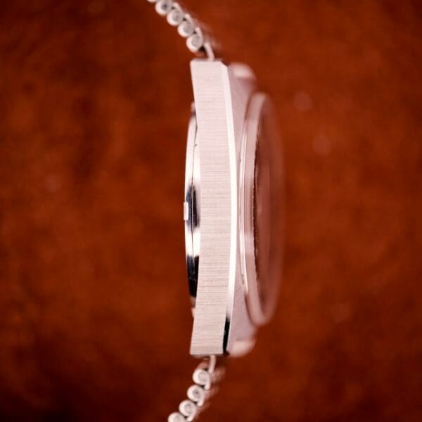 Close-up side view of the silver Hamilton Automatic HF-36 Day-Date Hi-Beat Cal. 631 wristwatch against a blurred brown background.