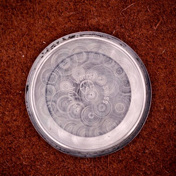 A metallic, circular Hamilton Automatic HF-36 Day-Date Hi-Beat Cal. 631 with etched concentric circles is displayed on a textured brown surface.