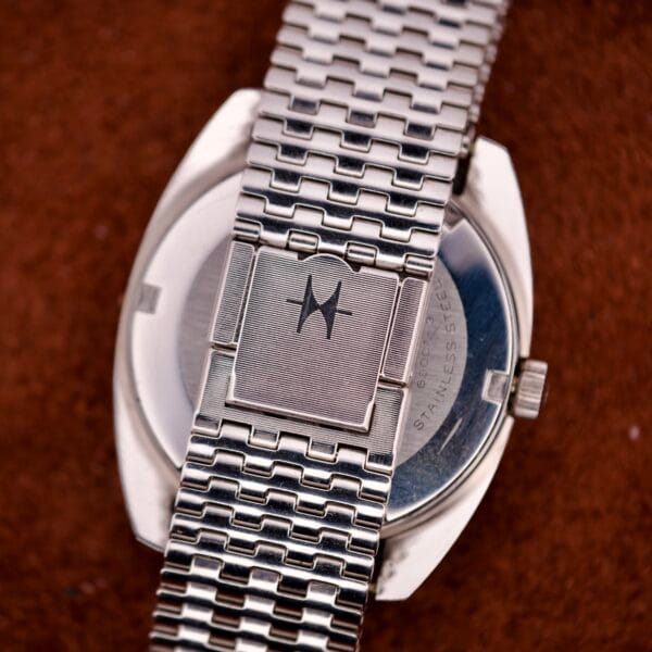 Close-up of the silver metal band with a star logo on the clasp, resting on brown fabric—an elegant detail from the Hamilton Automatic HF-36 Day-Date Hi-Beat Cal. 631 timepiece.