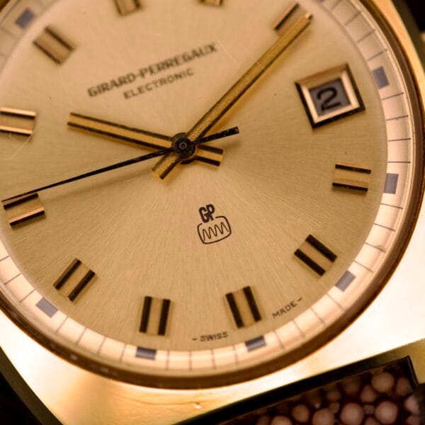 Close-up of the Girard Perregaux Electronic Ref. 9280 6H Large Cushion Case watch, featuring a gold face with black and gold hour markers, and displaying time and date.