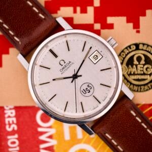An Omega Automatic Seamaster Ref. 166.020 For "U.S. Steel" Cal. 1010 Full Set wristwatch with a brown leather strap and date display, shown on a red and gold background.