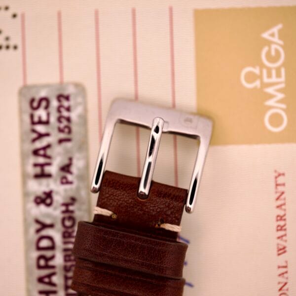 A brown leather strap with a silver buckle, displayed on Omega warranty papers—ideal for your Omega Automatic Seamaster Ref. 166.020 "U.S. Steel" Cal. 1010 Full Set or similar models with Cal. 1010 movements.