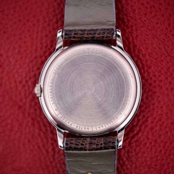 The back of a Hamilton Thin-o-matic T-500 with Caliber 666 Automatic Micro-Rotor and leather strap, shown resting on a textured red surface.