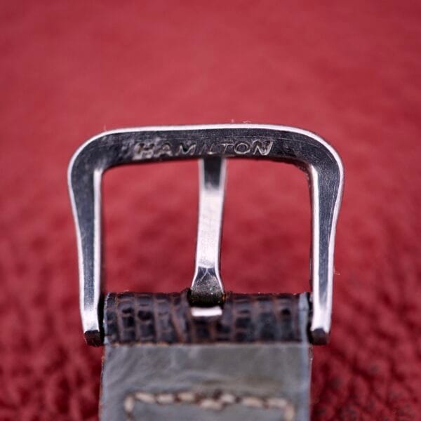 Close-up of a metal buckle engraved with HAMILTON on a textured leather strap—a refined detail of the Hamilton Thin-o-matic T-500 Caliber 666 Automatic Micro-Rotor.