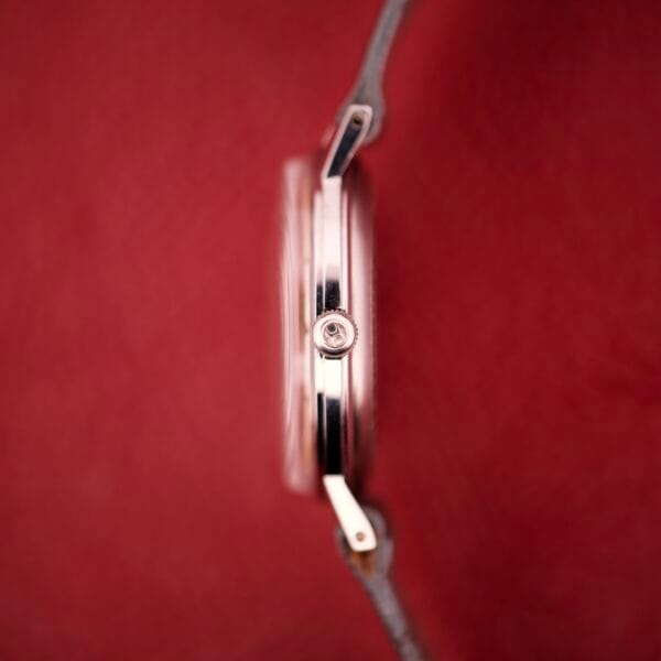 A side view of the Hamilton Thin-o-matic T-500 Caliber 666 Automatic Micro-Rotor wristwatch with a brown leather strap, set against a vibrant red background.