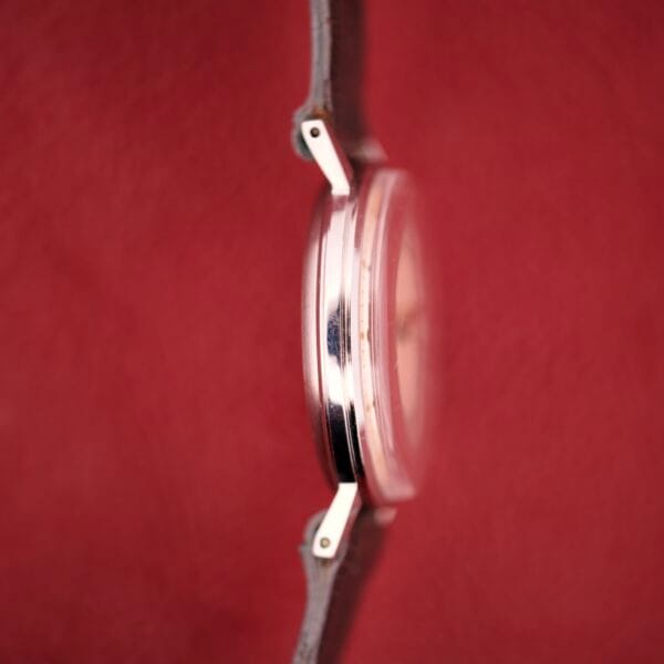 A close-up side view of the Hamilton Thin-o-matic T-500 Caliber 666 Automatic Micro-Rotor wristwatch with a brown strap, set against a vibrant red background.