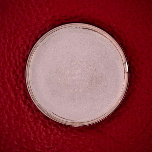 A round, silver metal case back with faint engraving, likely from a Hamilton Thin-o-matic T-500 Caliber 666 Automatic Micro-Rotor, placed on a textured red surface.