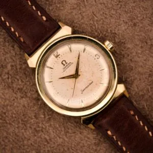 An Omega Automatic Seamaster Ref. 14363 with 14k gold capped bull horn lugs and a brown leather strap rests on a textured brown surface.