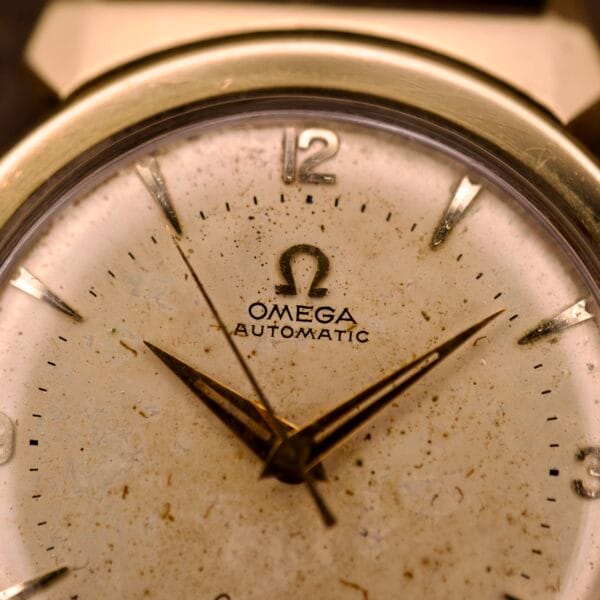 Close-up of an Omega Automatic Seamaster Ref. 14363 watch face featuring gold hands, 14k gold capped bull horn lugs, and visible signs of aging.