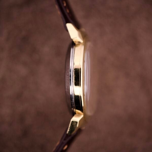 Close-up side view of the Omega Automatic Seamaster Ref. 14363, featuring 14k gold capped bull horn lugs and a brown leather strap against a rich brown background.