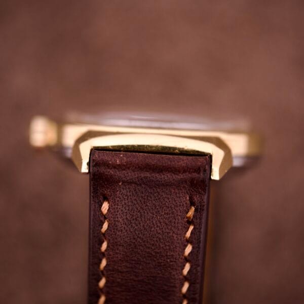 Close-up of a brown leather strap with beige stitching and Bull Horn Lugs, paired with the Omega Automatic Seamaster Ref. 14363 14k Gold Capped in the background.