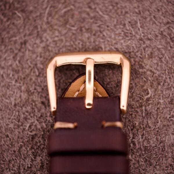Close-up of an Omega Automatic Seamaster Ref. 14363 with 14k gold capped bull horn lugs, attached to a brown leather strap, displayed on a textured fabric background.