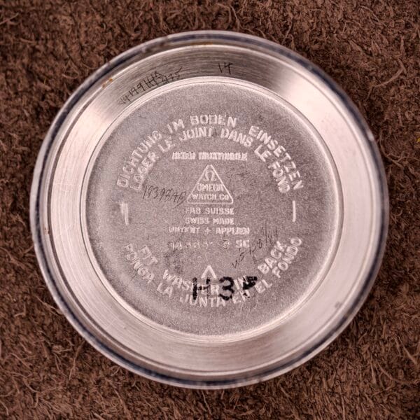 Close-up of the Omega Automatic Seamaster Ref. 14363 14k Gold Capped case back, featuring engraved text and numbers on a brown textured surface, highlighting its distinctive Bull Horn Lugs.