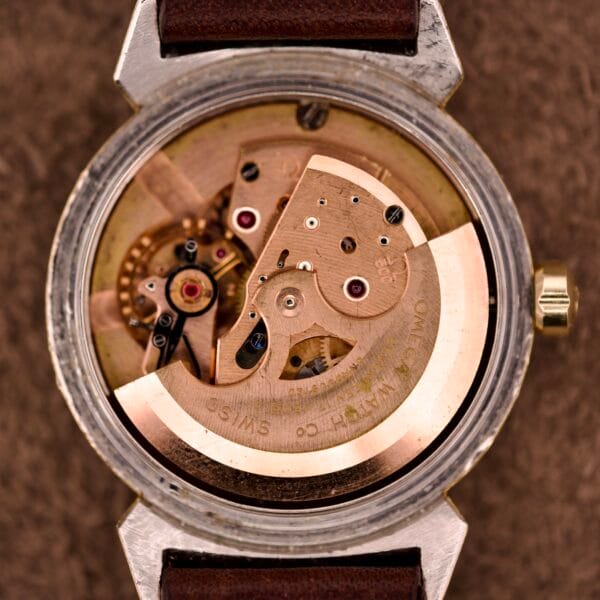 Close-up of an Omega Automatic Seamaster Ref. 14363 featuring exposed mechanical movement, bull horn lugs, and a brown leather strap in 14k gold capped finish.