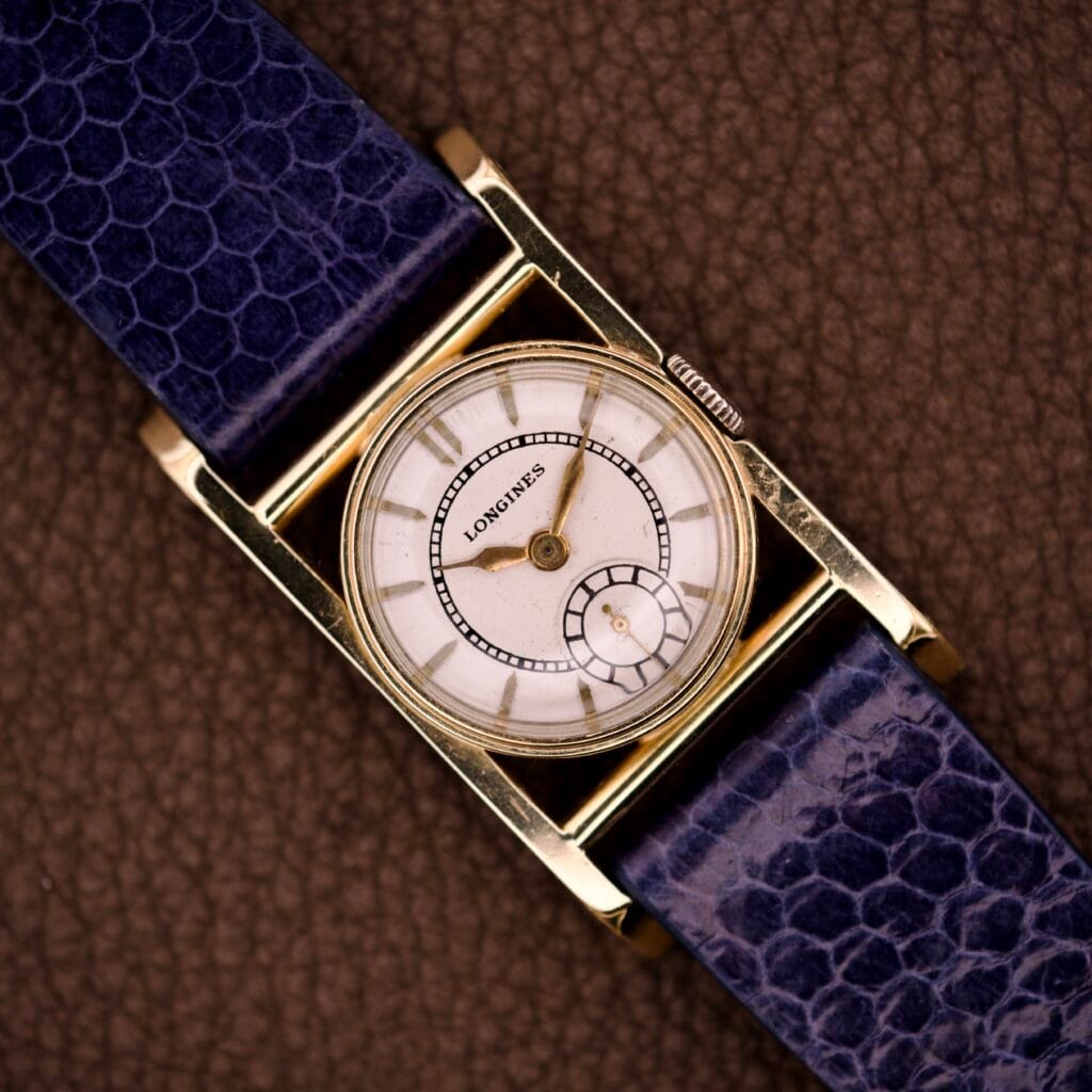 Longines Mainliner Art Deco Drivers Watch Manual Wind Cal. 8L with a gold rectangular case, white dial, and blue textured leather strap shown on a brown background.