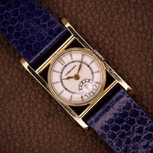 Longines Mainliner Art Deco Drivers Watch Manual Wind Cal. 8L with a gold rectangular case, white dial, and blue textured leather strap shown on a brown background.