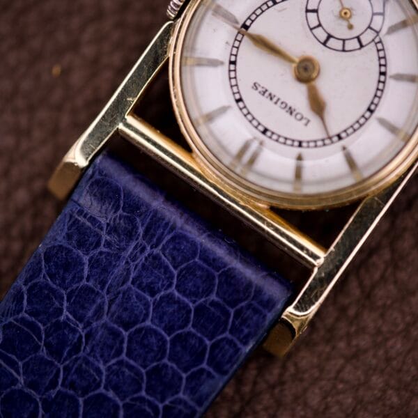 Close-up of a vintage Longines Mainliner Art Deco Drivers Watch Manual Wind Cal. 8L with a blue textured leather strap on a brown surface.