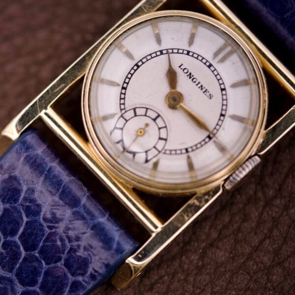 Close-up of a Longines Mainliner Art Deco Drivers Watch Manual Wind Cal. 8L with a blue textured strap and gold casing on a brown surface.