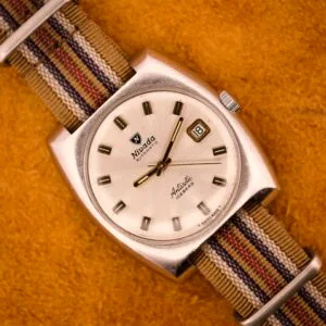 A Nivada Automatic Antarctic Iceberg Date Ref. 4297 with a sunburst dial and striped fabric strap, shown on an orange textured surface.