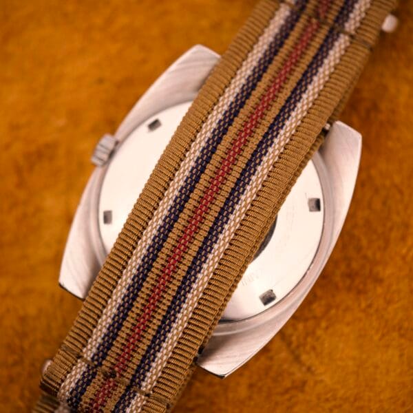 A close-up of the Nivada Automatic Antarctic Iceberg Date Ref. 4297 with a sunburst dial and striped fabric NATO strap, resting on a brown textured surface.