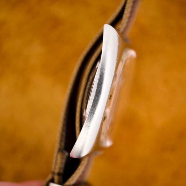 Side view of the Nivada Automatic Antarctic Iceberg Date Ref. 4297 with a silver case, sunburst dial, and tan fabric strap set against a blurred orange background.