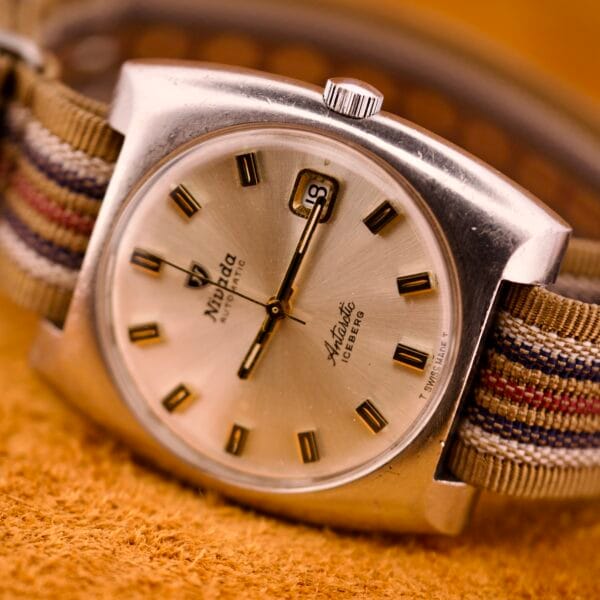 The Nivada Automatic Antarctic Iceberg Date Ref. 4297 features a sunburst dial, striped fabric band, gold hour markers, and a date display.