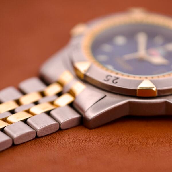 Close-up of the Tag Heuer 1500 Series Blue Sunburst Dial Ref. WD 1221-K-20, featuring a two-tone metal band, shown on a brown leather surface.