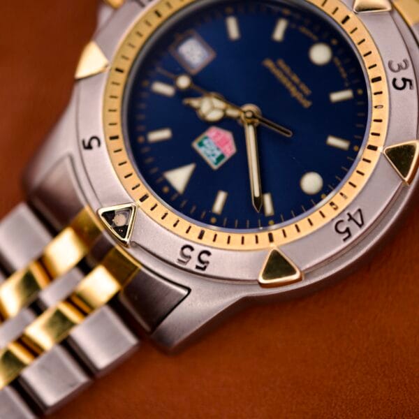 Close-up of a Tag Heuer 1500 Series Ref. WD 1221-K-20 wristwatch with a blue sunburst dial and gold accents, shown on a brown surface.