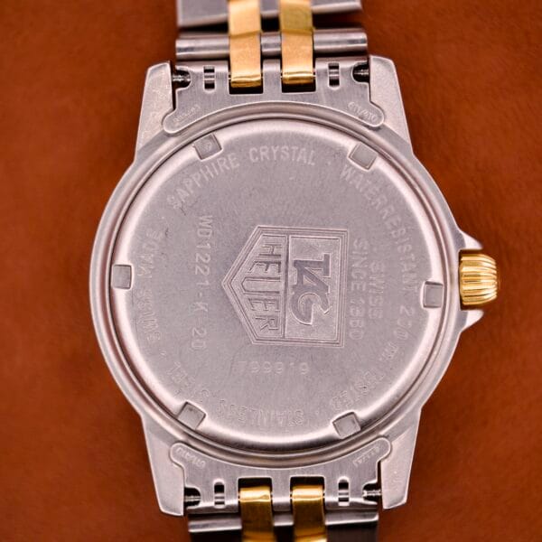 Back of a Tag Heuer 1500 Series Blue Sunburst Dial Ref. WD 1221-K-20, featuring engraved details and a silver and gold metal bracelet, displayed on a brown background.