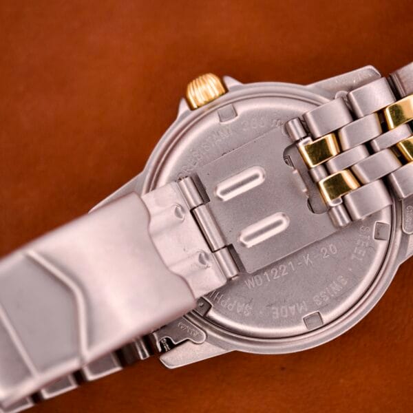 Close-up of the back of a Tag Heuer 1500 Series Blue Sunburst Dial Ref. WD 1221-K-20 wristwatch, featuring a metal band with gold accents, displayed on a brown surface.