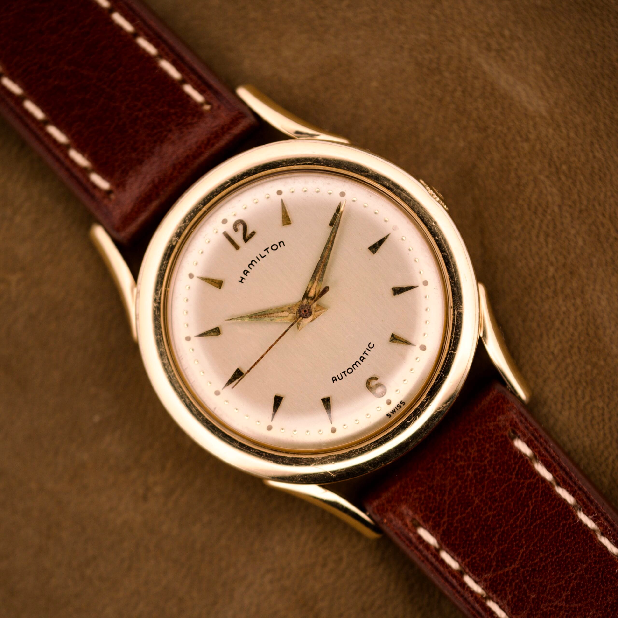 Hamilton Automatic Ref. K-407 wristwatch with a Cal. 661 movement and 10k gold filled case, shown with a brown leather strap on a brown textured surface. Hamilton Automatic Ref. K-407 wristwatch with a Cal. 661 movement and 10k gold filled case, shown with a brown leather strap on a brown textured surface.