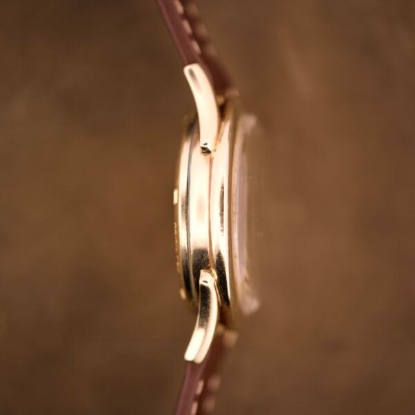 Side view of a Hamilton Automatic Ref. K-407 with a 10k gold filled case, Cal. 661 movement, and brown leather strap set against a softly blurred brown background.