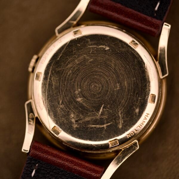 Close-up of a scratched 10k gold filled case back on a Hamilton Automatic Ref. K-407 (Cal. 661) watch with leather straps, highlighting circular wear marks.