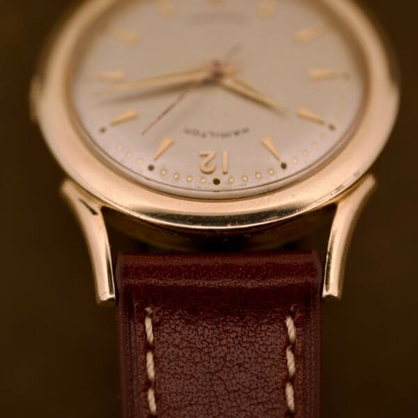 Close-up of a Hamilton Automatic Ref. K-407 wristwatch with a 10k gold filled case, brown leather strap, and cream-colored face featuring the number 12.