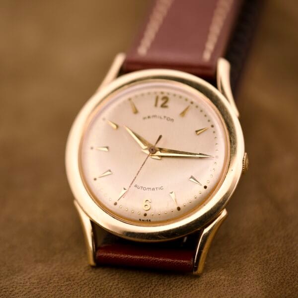 Hamilton Automatic Ref. K-407 wristwatch with a 10k gold filled case and brown leather strap, Caliber 661, displayed on a brown surface.