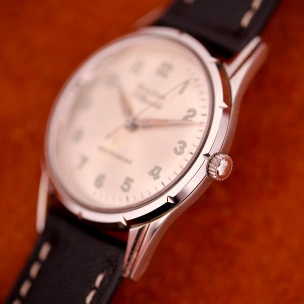 Close-up of a 1970 Bulova 23 Jewels wristwatch with self-winding Cal. 10BZAC movement, white face, stainless steel case, and black leather strap on a brown surface.