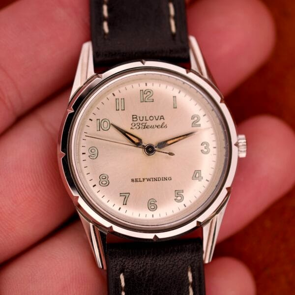 A close-up of a 1970 Bulova 23 Jewels Self-Winding Cal. 10BZAC wristwatch featuring a stainless steel case and sleek black leather strap.