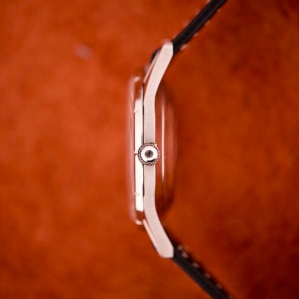 Side view of a 1970 Bulova 23 Jewels Self-Winding Cal. 10BZAC wristwatch with black strap, stainless steel case, and crown, set against a reddish-brown background.