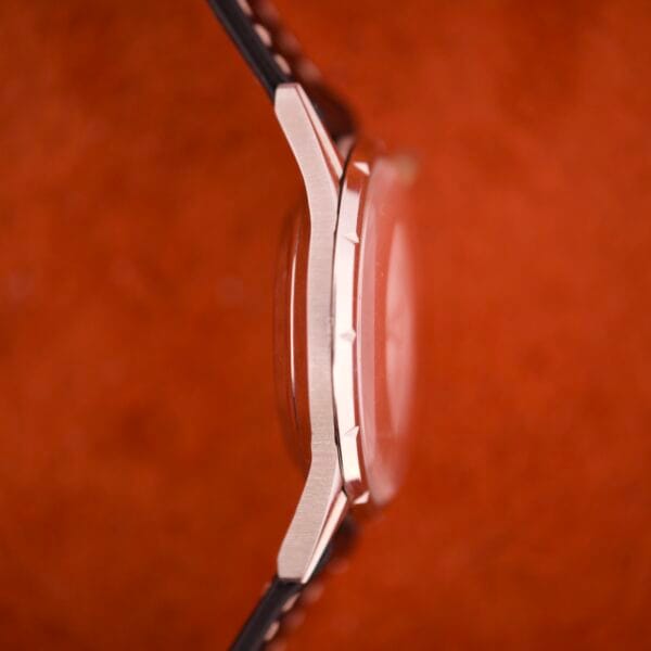 Side view of the 1970 Bulova 23 Jewels Self-Winding Cal. 10BZAC wristwatch with a stainless steel case and black strap, set against a textured red background.