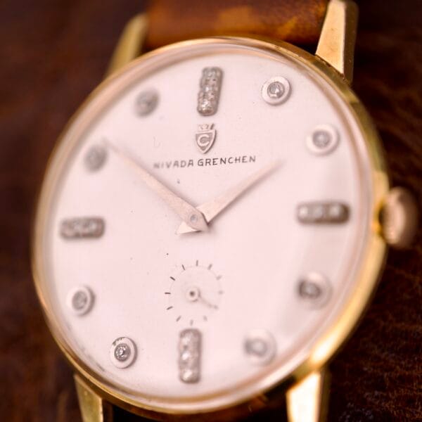 Close-up of a Nivada Grenchen Manual Wind Cal. R34 wristwatch featuring a white dial, diamond markers, and a brown leather strap.