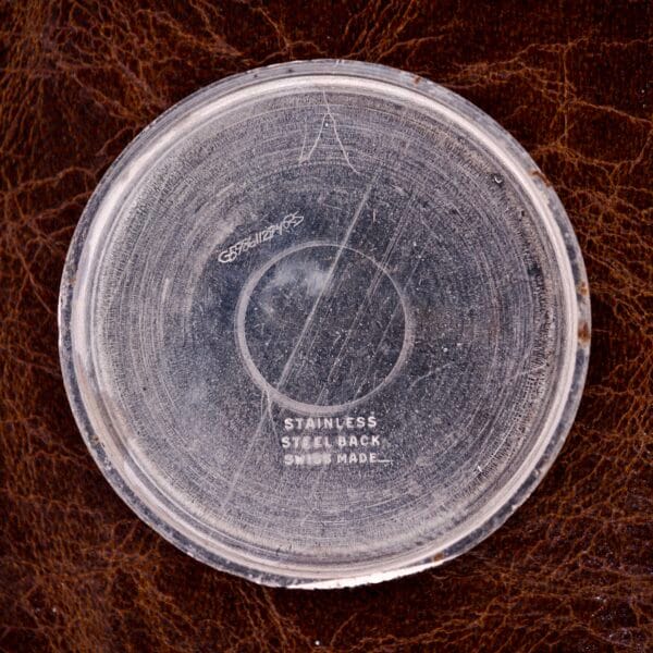 A scratched metal back marked Stainless Steel Back, Swiss Made, suggests a Nivada Grenchen Manual Wind Cal. R34 with a white dial and diamond markers on brown textured leather.