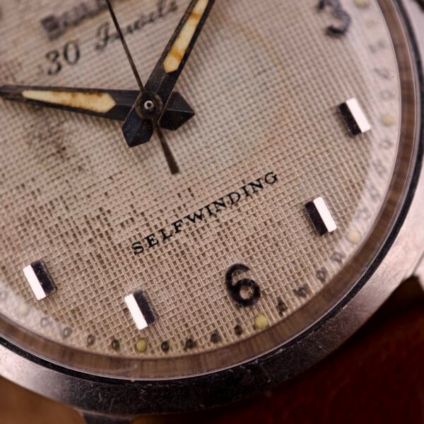 Close-up of a Bulova 30 Jewels Automatic Cal. 10COAC watch face, featuring SELFWINDING text and an aged waffle-textured dial in a stainless steel case.