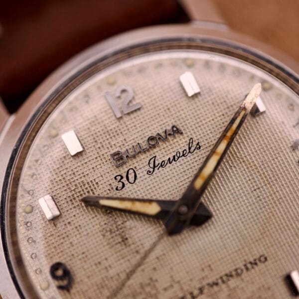 Close-up of the Bulova 30 Jewels Automatic Cal. 10COAC, featuring a classic waffle dial and stainless steel case, with worn hour and minute hands visible.