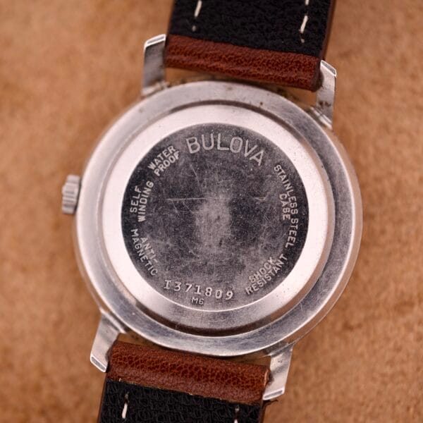 Close-up of the back of a Bulova 30 Jewels Automatic Cal. 10COAC wristwatch featuring a waffle dial, stainless steel case, leather strap, and engraved text.