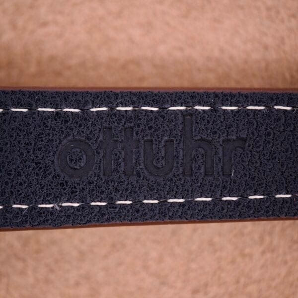 Close-up of a black leather strap with white stitching, embossed with "ottuhr," paired with a Bulova 30 Jewels Automatic Cal. 10COAC featuring a textured Waffle Dial and stainless steel case.