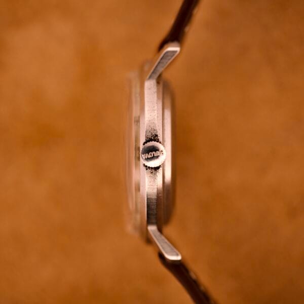 Close-up side view of a Bulova 30 Jewels Automatic Cal. 10COAC watch with a waffle dial and stainless steel case, set against a brown background.