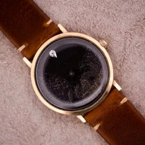 A 1970s Longines manual wind wristwatch with a black dial featuring diamond markers and a brown leather strap rests on a beige textured surface.