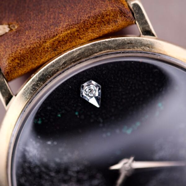 Close-up of a 1970s Longines manual wind wristwatch featuring a black dial with a diamond marker and a worn brown leather strap.