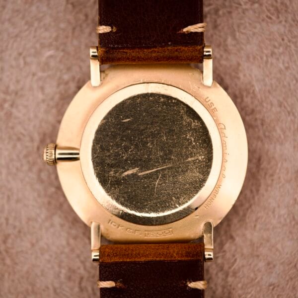 Close-up of the scratched back of a 1970s Longines Manual Wind Black Dial With Diamond Marker wristwatch with a brown leather strap, resting on a soft surface.