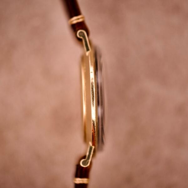 A close-up side view of a 1970s Longines Manual Wind watch, featuring a black dial and diamond marker, with a brown leather strap against a soft, blurred background.